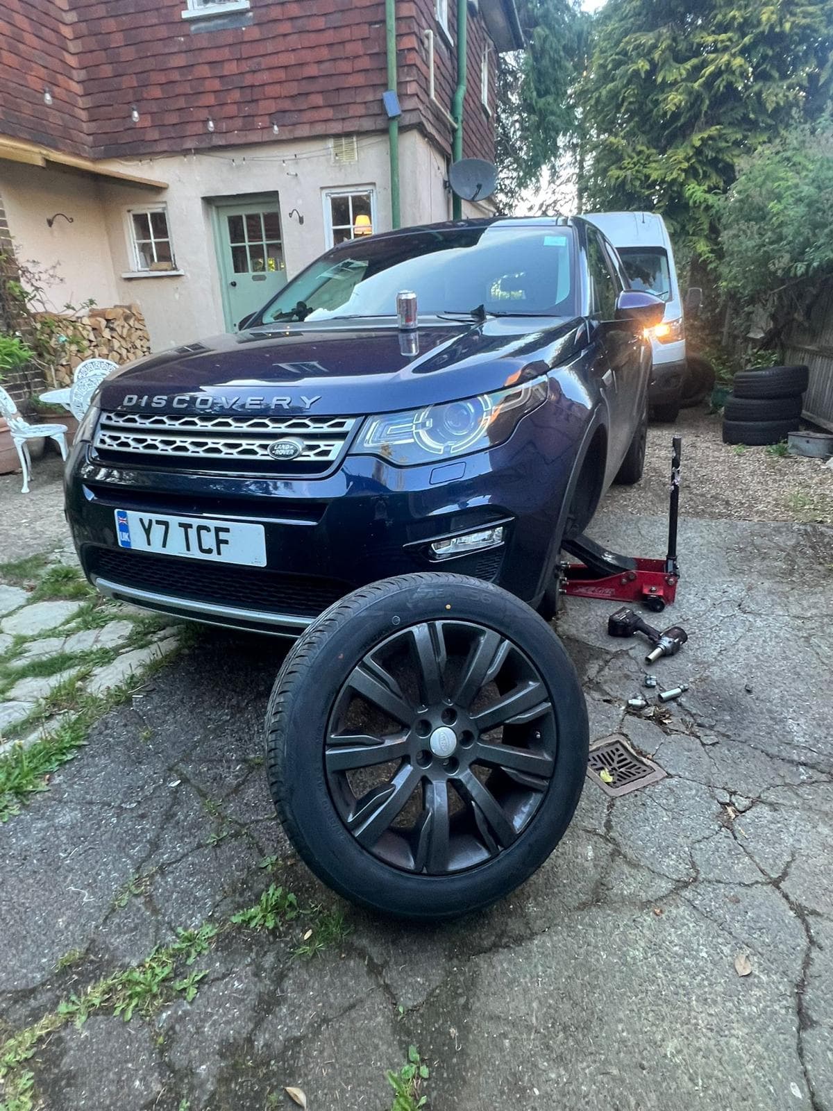 Mobile tyre fitter replacing a tyre on a driveway with a service van parked behind the vehicle